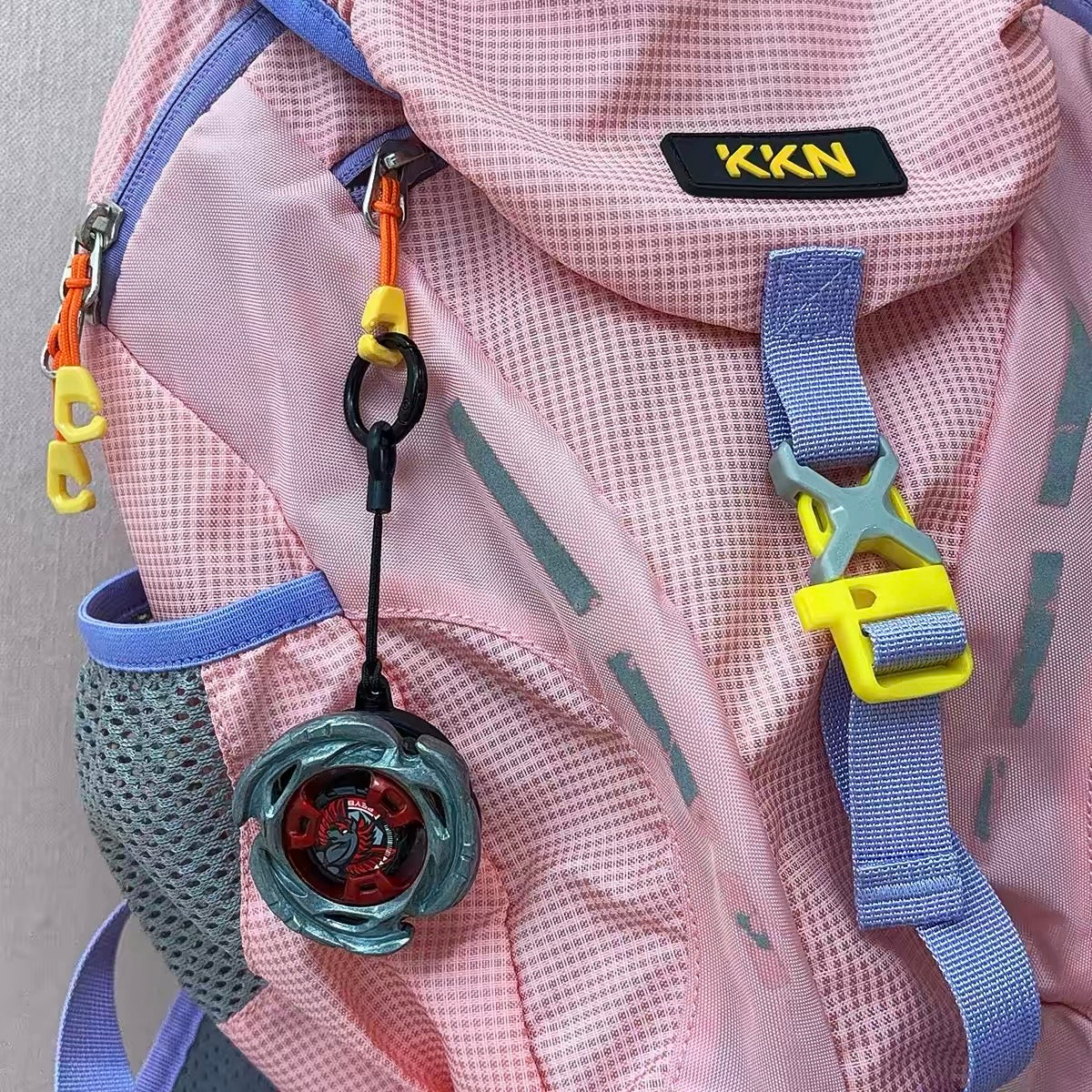 Beyblade keychain clipped to a backpack with a different blade installed